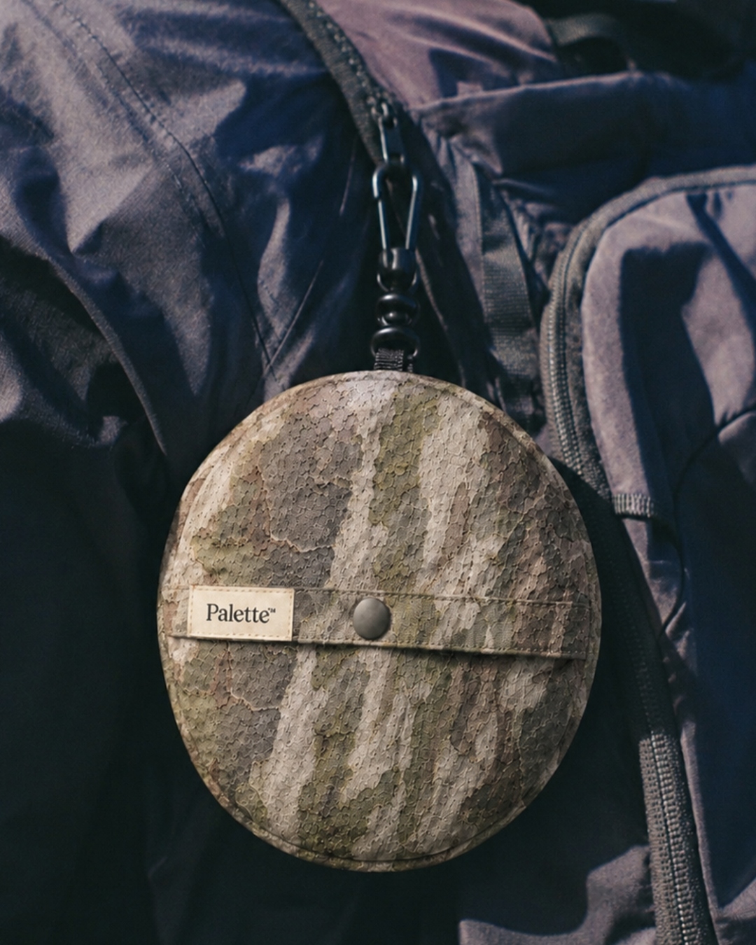 Packable system — camo cap stowed in carry pouch clipped to pack